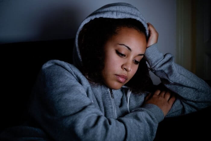 Pale african lady in blue grey hoodie, head in hands looking down - worrying about my health