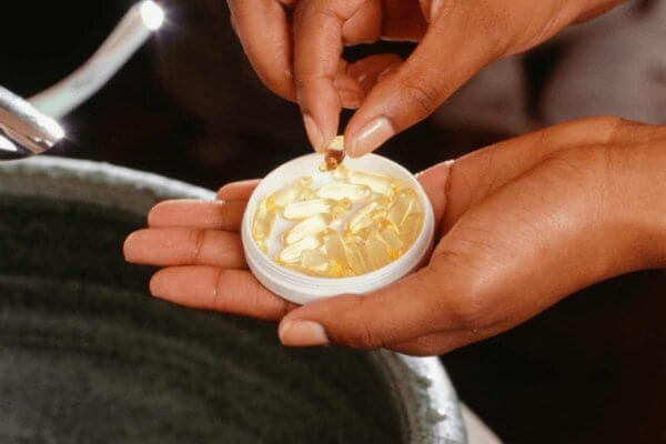 Pair of hands of african background holding a cup with some Vitamin D Pills and Covid-19