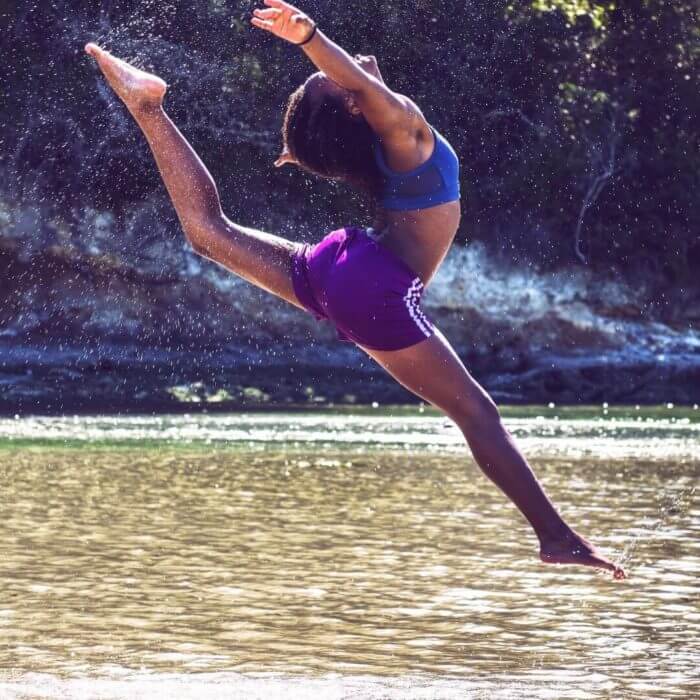 An athletic african woman jumping in a stream