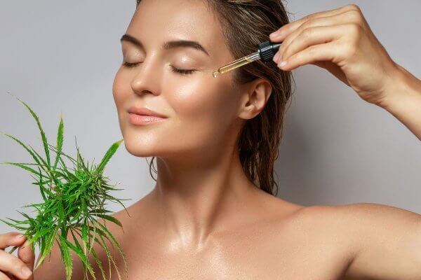 Skin benefits of CBD- showing lady with clear skin applying CBD oil from a dropper to her face.