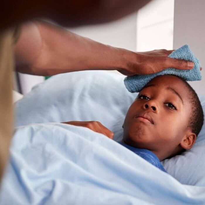 Young african boy in bed with fever, having his head sponged.