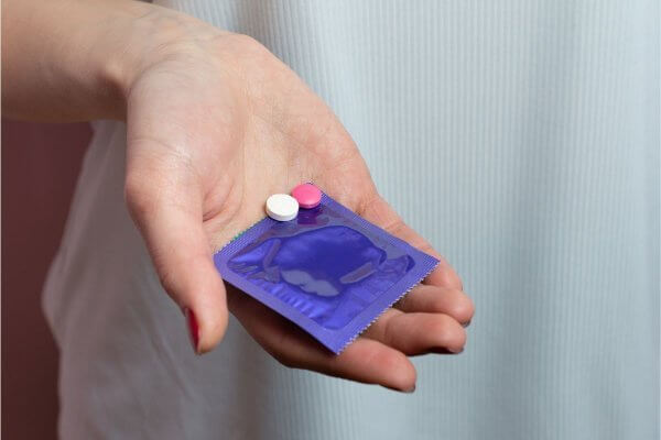 A hand holds out options for safe sex - a purple wrapped condom with Post pill or Postinor 2
