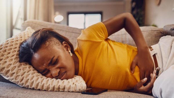 Lady of african origin wearing a yellow blouse lying on the sofa in endometriosis pain