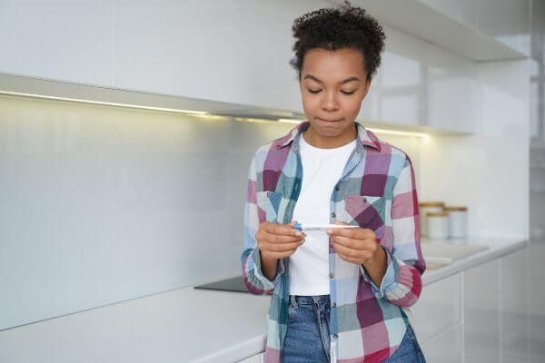 Young black lady holding a pregnancy test waiting to see if taking Postinor 2 worked