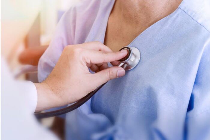 Image of clinician placing a stethoscope on the chest if a long covid patient to examine heart and lungs