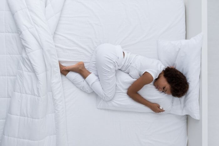 Lady of african origin lying in a bed with white bedsheets - Doctors believe rest and adjusting to a slower pace of life are key to recovery from long covid