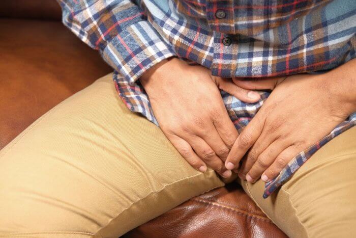 Causes of Male Infertility - Image of a man seated while placing both hands on his groin