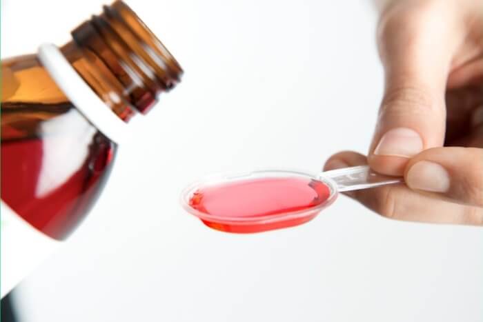 Holding a spoon filled with medicine from a bottle of cough medicine