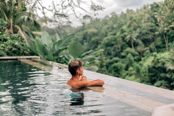 Serenity and peace often coes at a ental wellness aied retreat - man in prayerful pose while bathing in a Bali infinity pool