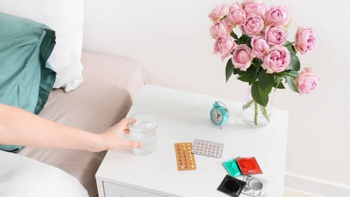 Best Non Hormonal Birth Control Option image of lady's hand reaching for a glass of water with some pills and condoms on the top