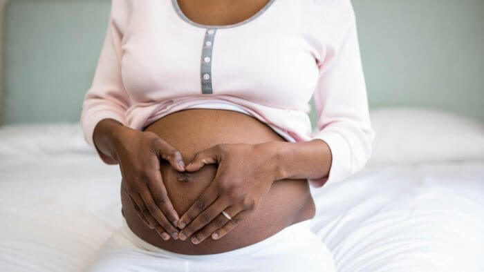 Africal lady making a heart sign on her pregnant abdomen