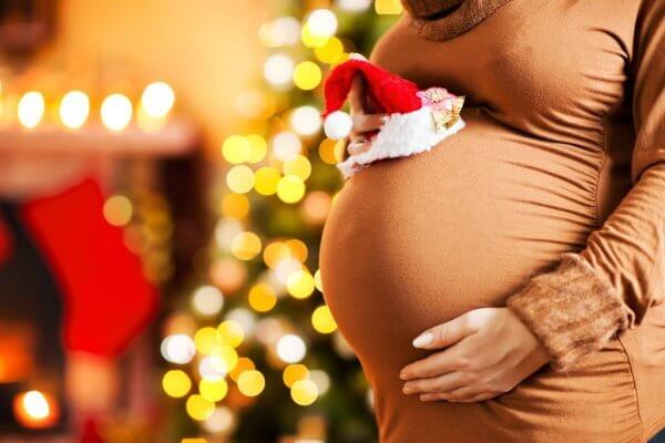 Pregnant lady holding a santa hat over her bump At Christmas