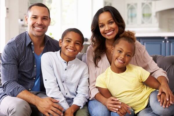 Family of four, african background - mum, dad, son and daughter, casually dressed while sitting on sofa - In your family its important to gauge when to talk to your kids about sex