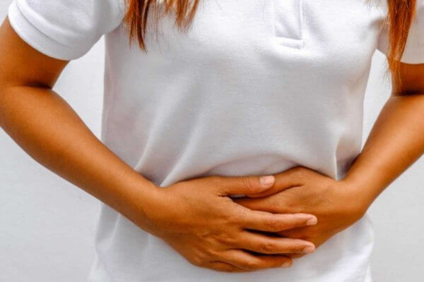 Lady in white tee shirt holding her abdomen from stomach cramps, one of the bowel-related problems from Covid19
