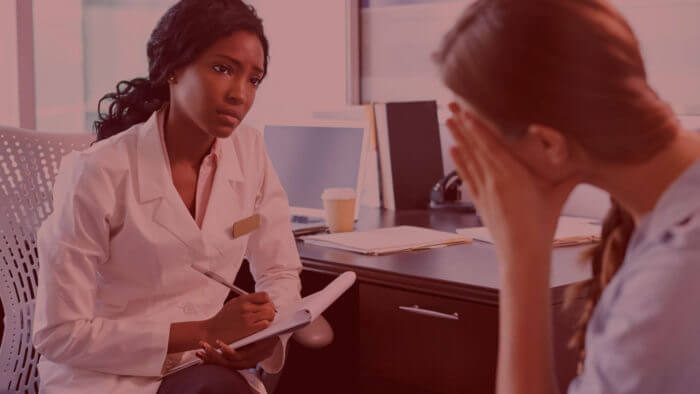 Femal doctor of african origin dressed in a white coat speaking sympathetically to a patient about best remedy for stomach ulcer