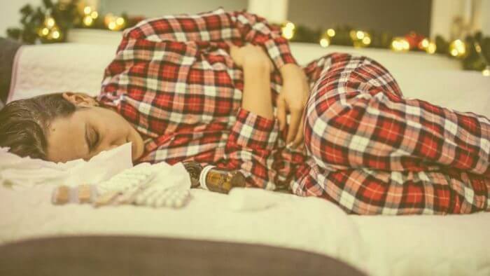 Lady of afrocarribbean origin in red stripped pajamas lying on a bed in obvious pain - possibly from a stomach ulcer