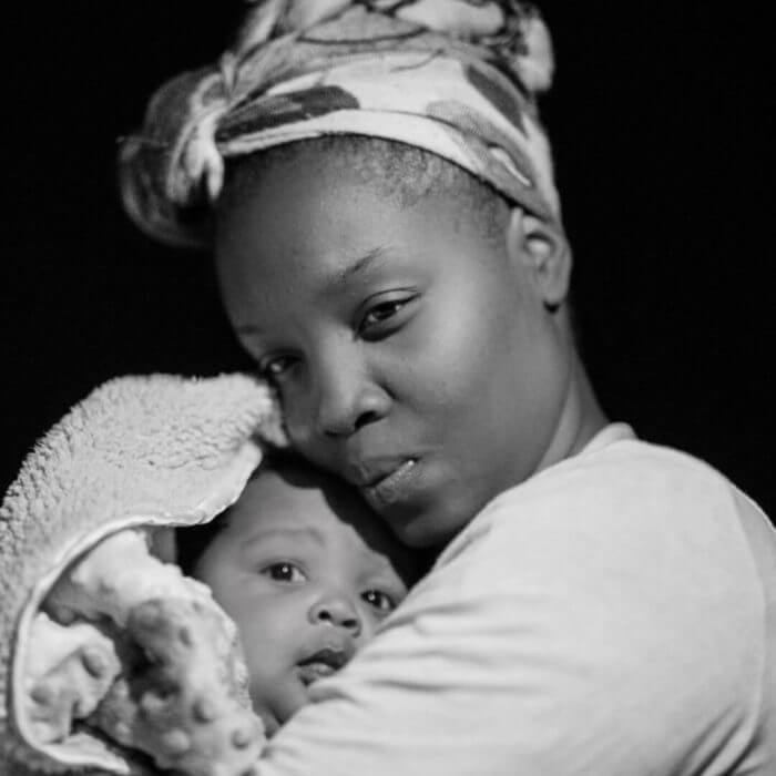 Photo of an african mother in head gear closely cradling her young baby.