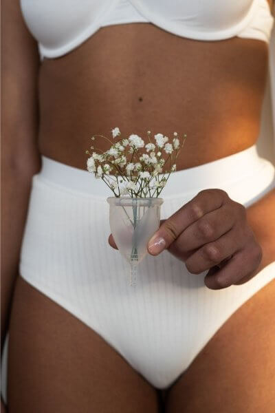 abnormal period image. Lady of African background in plain white underwear holding a menstrual cup with a spray of white flowers