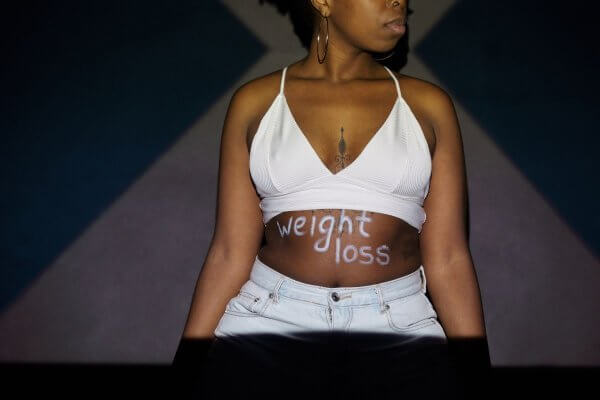 Pretty African lady in white bra-top and jeans  with weight loss written on her tummy after using ozempic for her weight loss journey