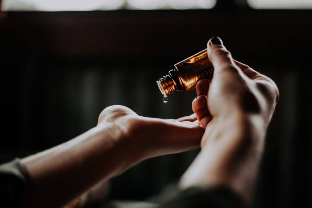 A pair of healing hands of a Natural Therapy Practitioner applying healing oil from a brown bottle. 