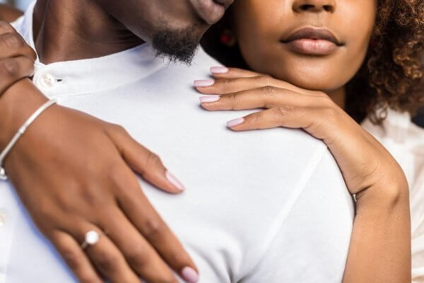 Young black couple embracing - her hand wearing her engagement ring prominent on his chest - regular contraception is more effective in the long term than emergency contraception