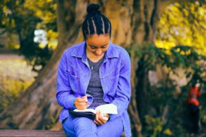 Haemoglobin C disease - african lady in blue deim coat and jacket with cornrows reading a book in a park.