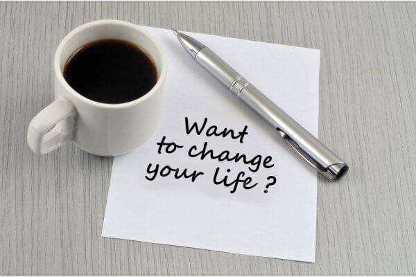 message in black script on white note paper beside a pen and cup of black coffee Want To Change Your Life?
