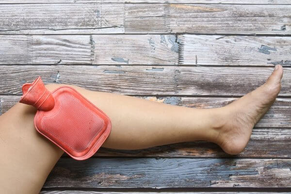 Image of bent knee with hot water bottle for relief of knee pain.