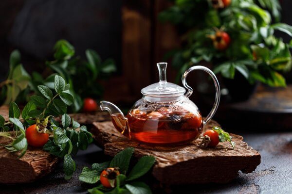 Clear glass kettle of Detox Tea on a table surrounded by green leaves and red fruits