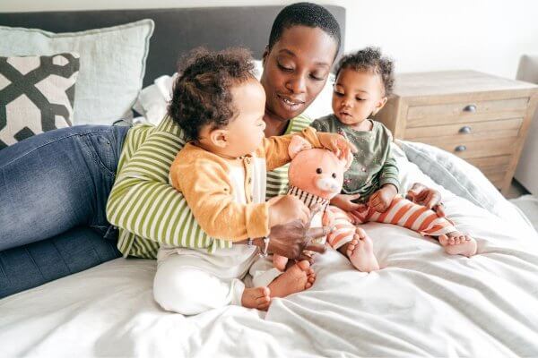 African mum playing with two young toddlers in bed, making time for family is living a balanced life