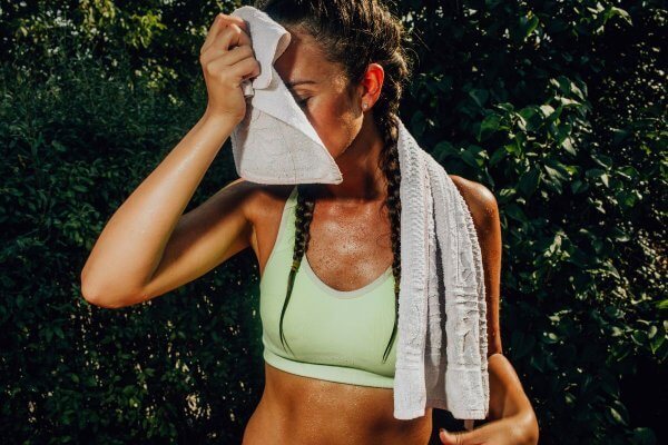 African lady in green crop top towelling her sweat soaked skin - ensure you have warmed u properly before starting the workout