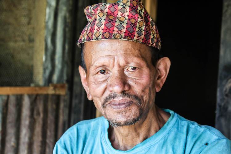 Picture of an older man of African backgound with a traditional cap and blue shirt.