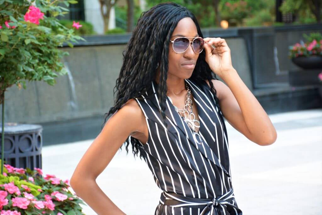 Young african lady in sunglasses and black striped dress looking boldly into the camera.
