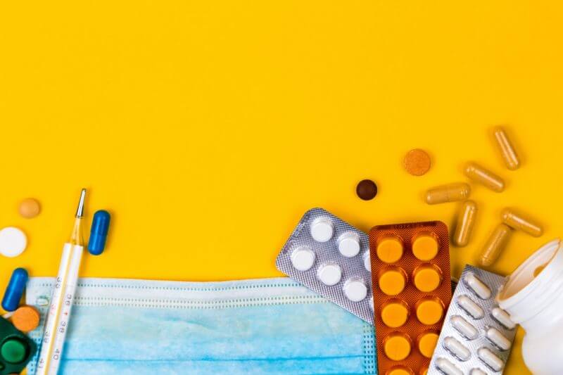 Understanding treatments for sickle cell anaemia - image of different pills, pill sachets, other drugs and face mask on a bright yellow background.